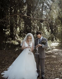 a bride and groom standing in a wooded area